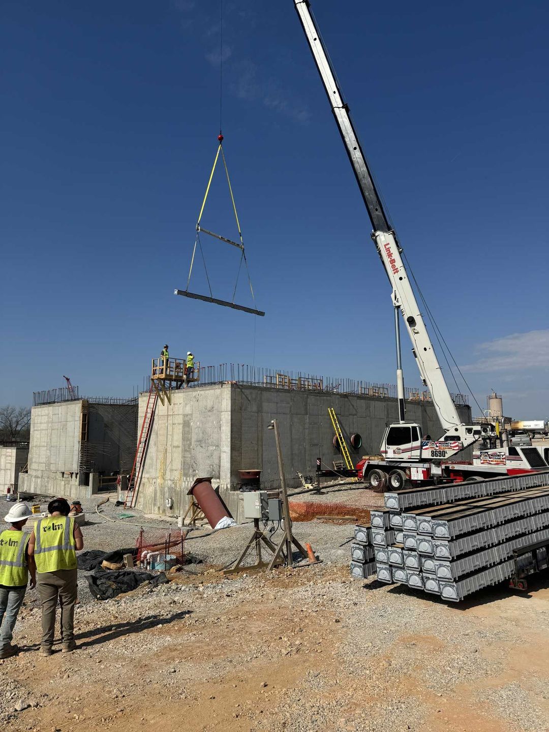 white crane lifting a concrete beam during construction on a sunny day.