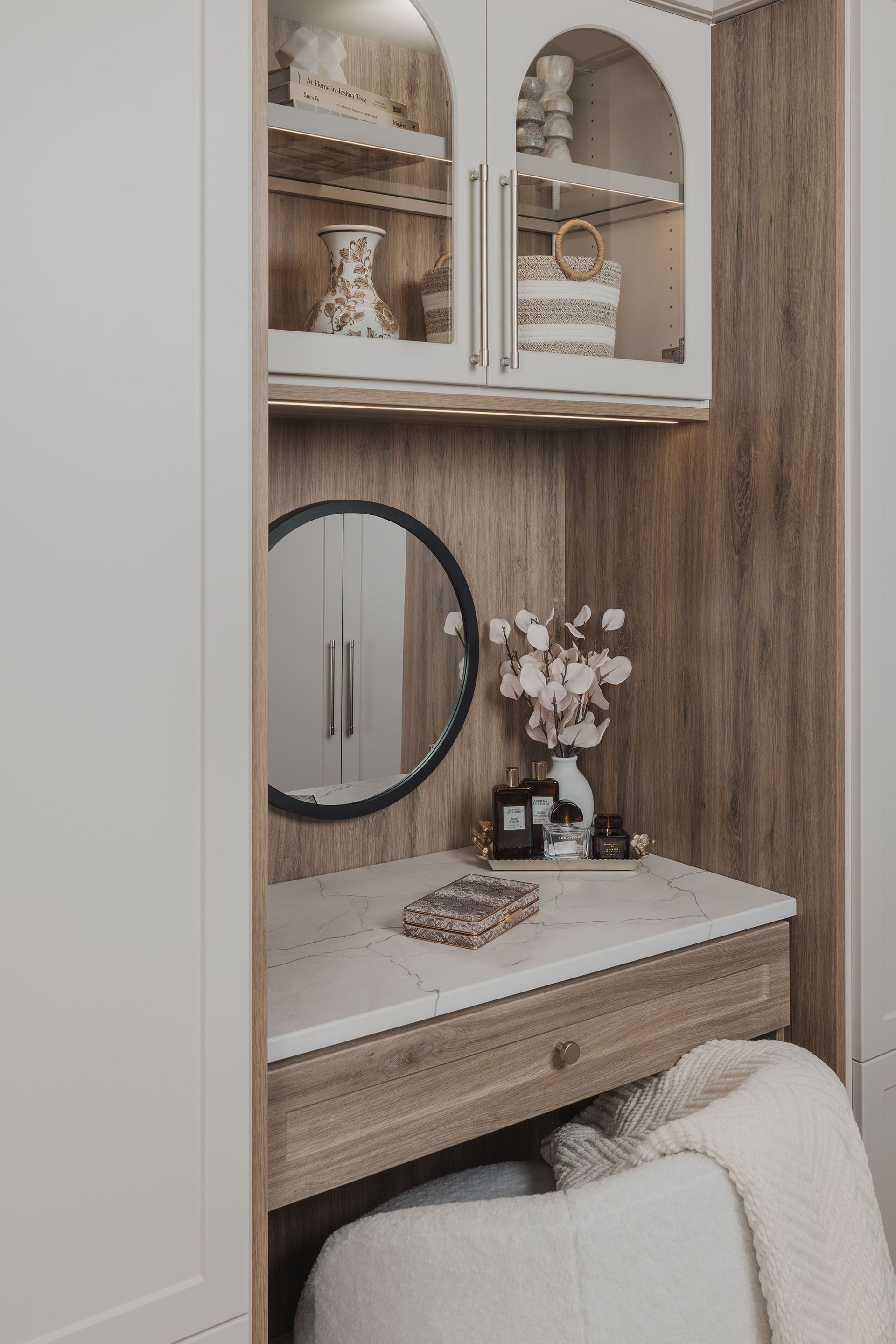 Built-in vanity nook with mirror, light wood cabinetry, white counter, and flowers on display