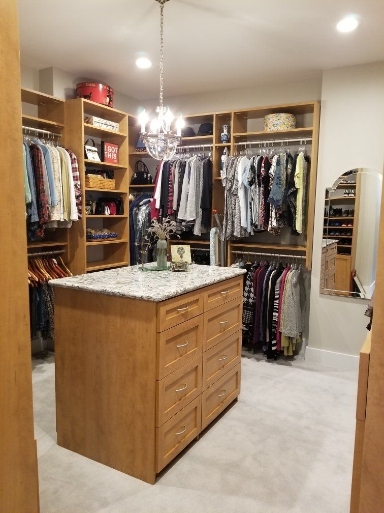 A walk in closet with lots of clothes and a large island in the middle.
