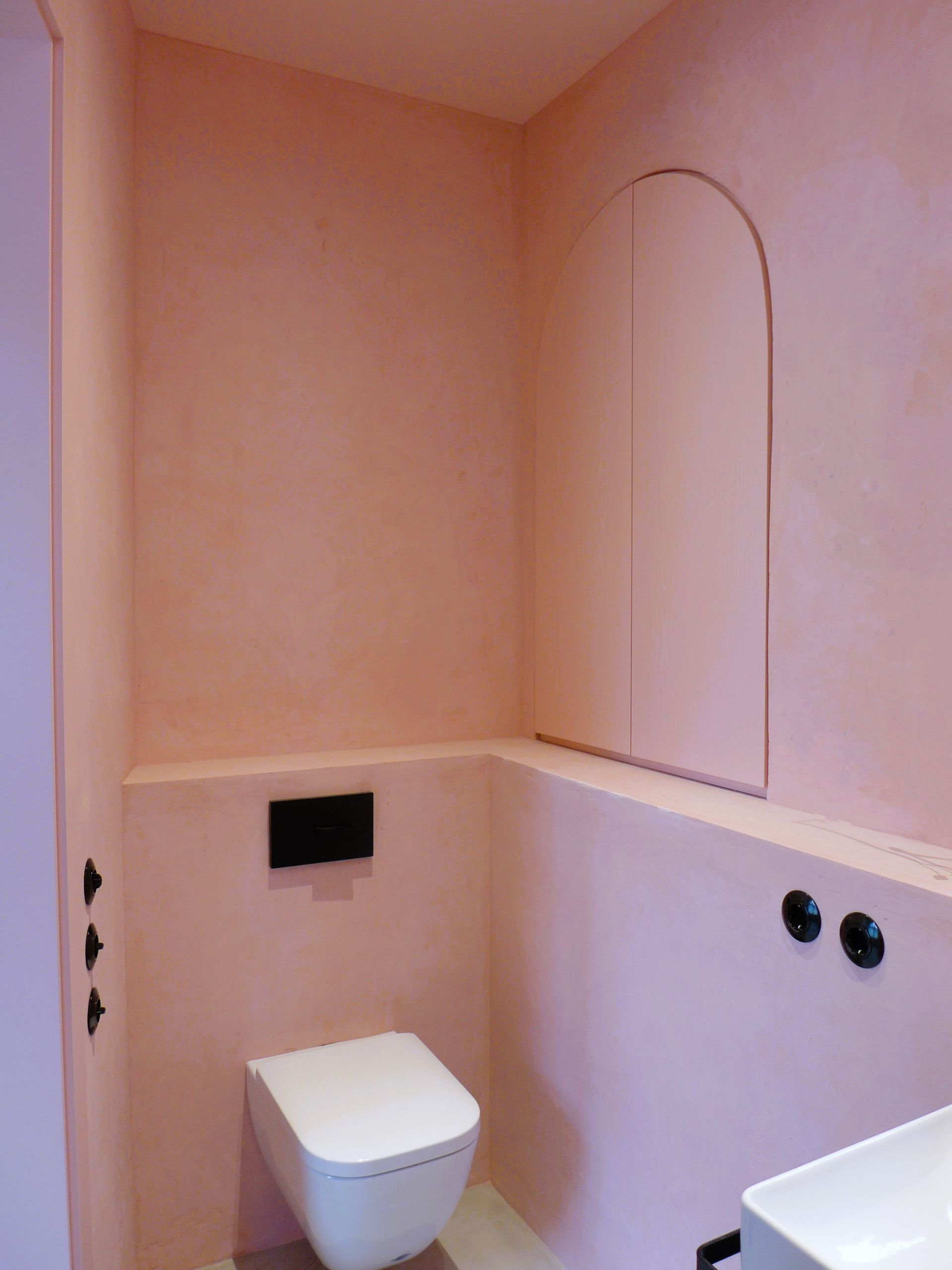 Ein Badezimmer mit rosa Wänden und einer weißen Toilette