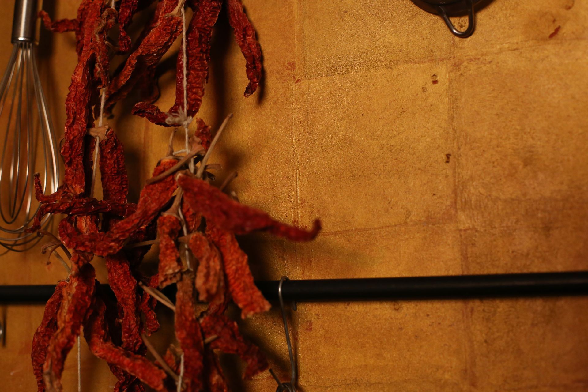 Ein Bündel getrockneter roter Paprika hängt neben einem Schneebesen an der Wand.