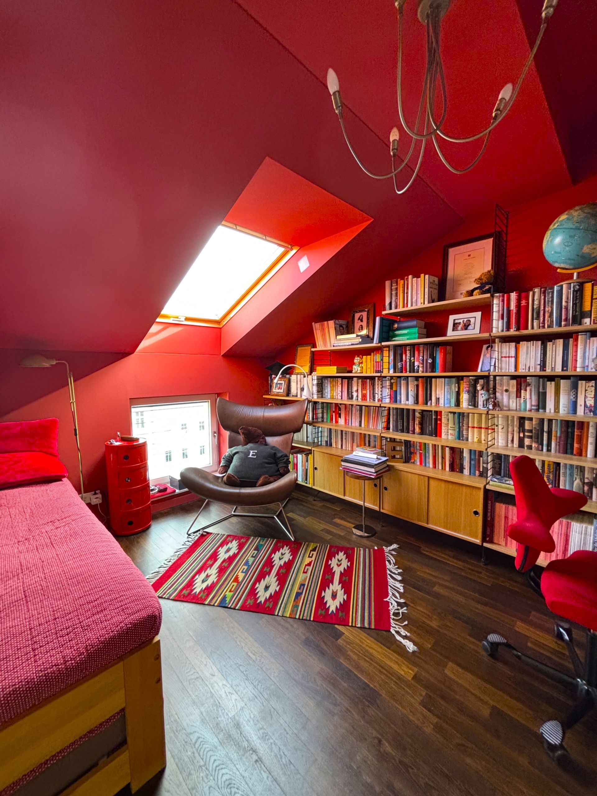 Dachgeschoss-Schlafzimmer mit leuchtend roten Wänden, Bücherregalen, einem Ledersessel, einem Teppich und einem roten Bett.