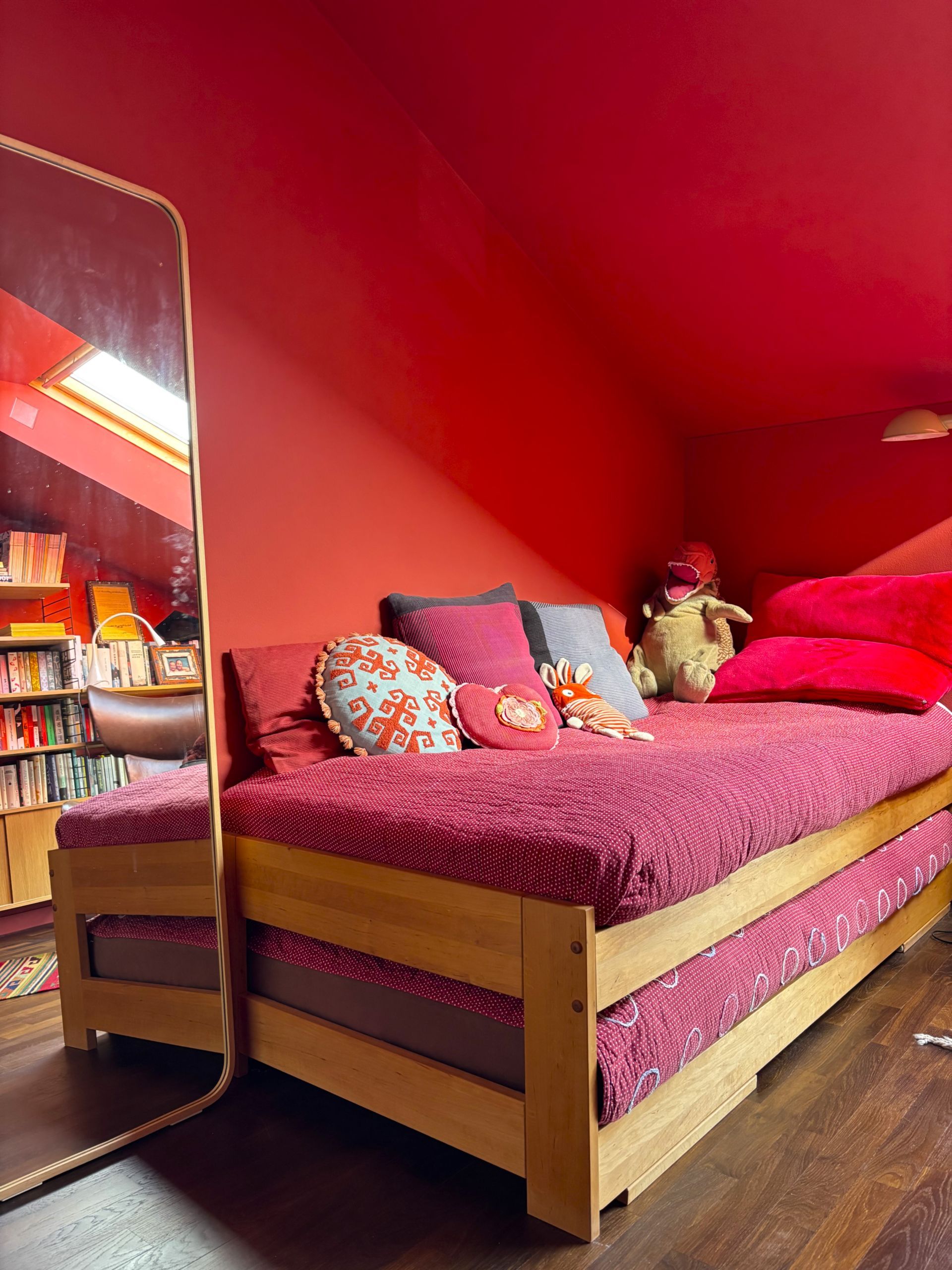 Ein Tagesbett mit rot gemusterter Bettwäsche und Zierkissen vor einer leuchtend roten Wand in einem Zimmer mit Spiegel.