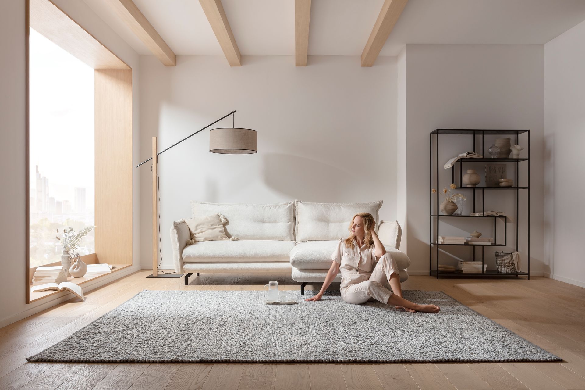 Eine Frau sitzt in einem Wohnzimmer neben einem weißen Sofa auf dem Boden.