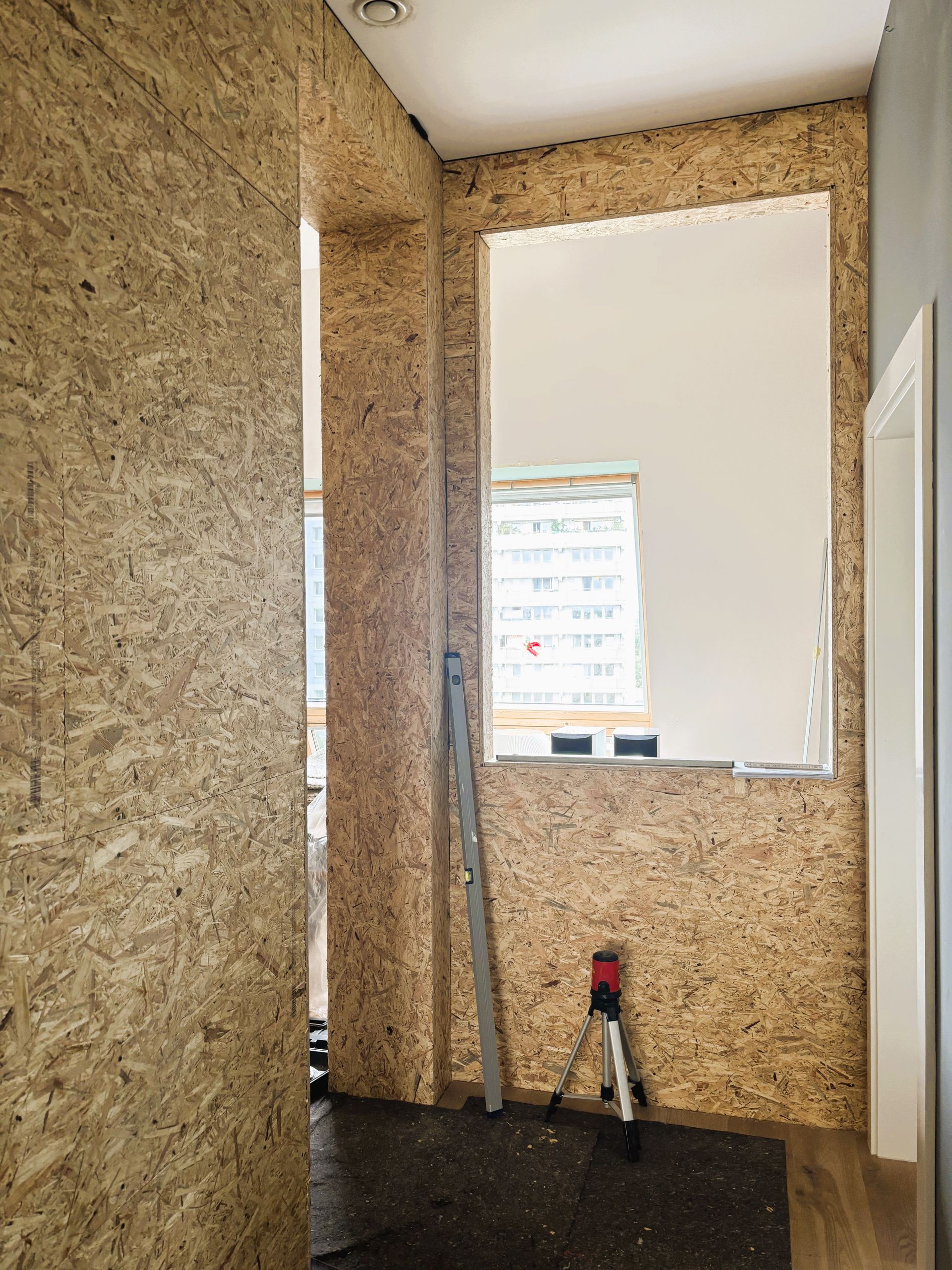 Ein Raum mit OSB-Holzvertäfelung an den Wänden, einem großen Einsatz und einem Laser-Nivelliergerät.
