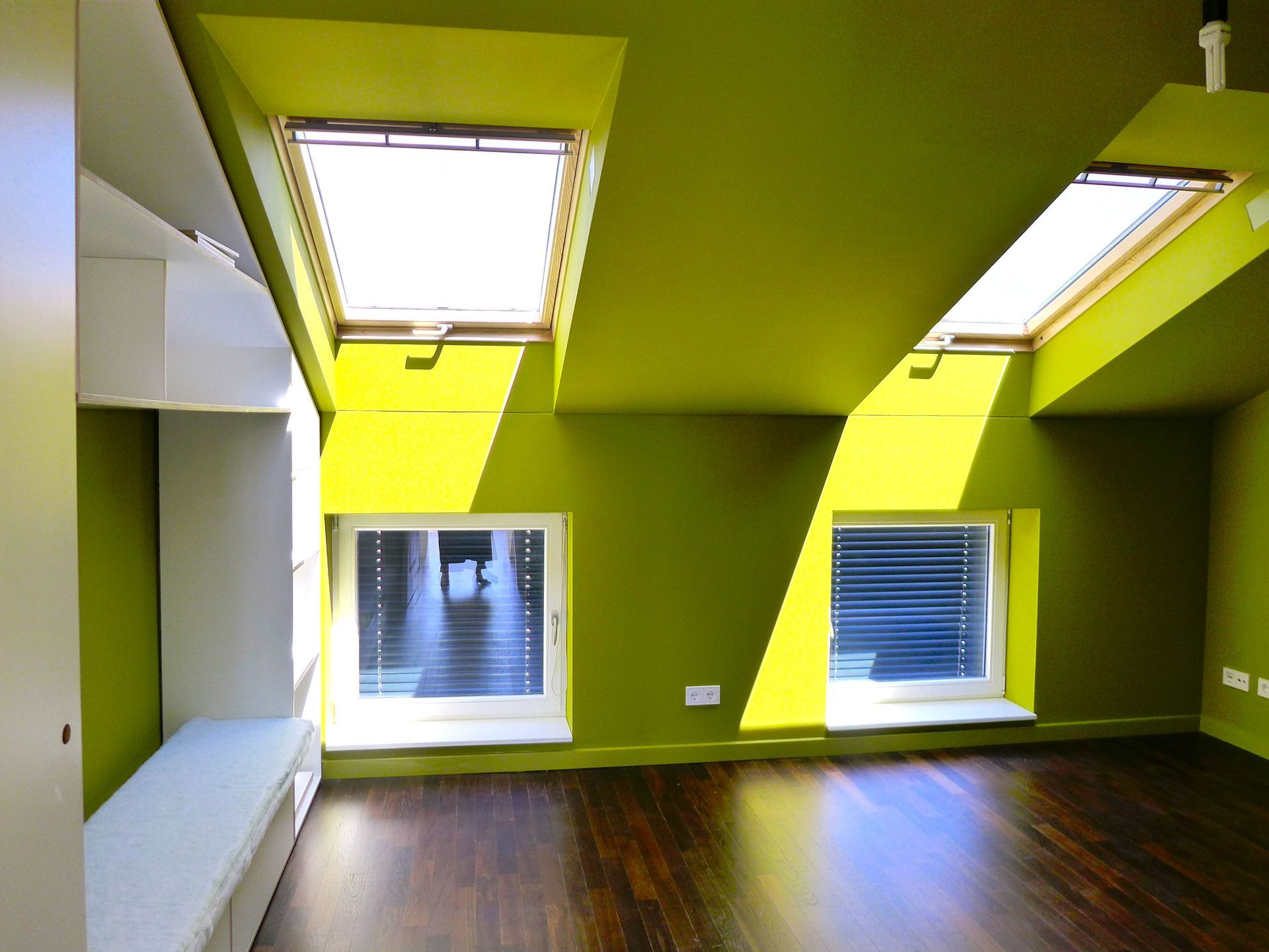 Dachzimmer mit lindgrünen Wänden, dunklen Holzböden, weißen Einbausitzbänken und vier Dachfenstern und Wandfenstern.