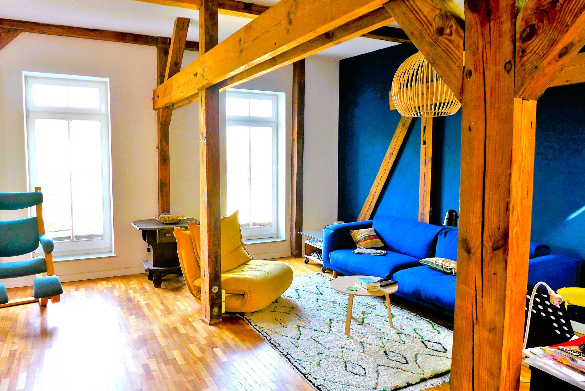 Ein Wohnzimmer mit einem blauen Sofa, einem gelben Sessel und Holzbalken.