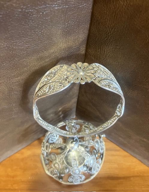 Ornate silver ring stand with floral design on a wooden surface against a brown backdrop