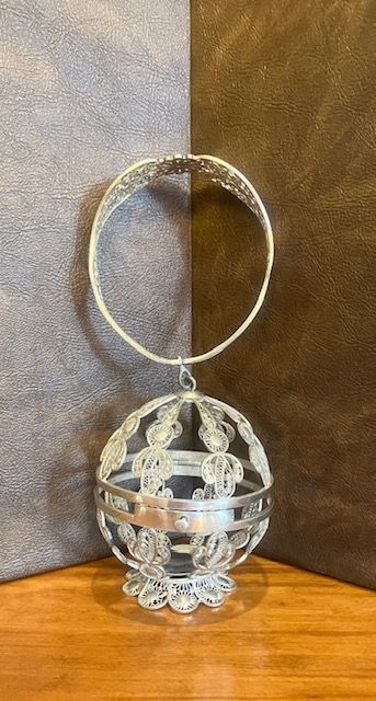 Decorative silver hanging ornament with a circular top ring and intricate filigree on a wooden surface