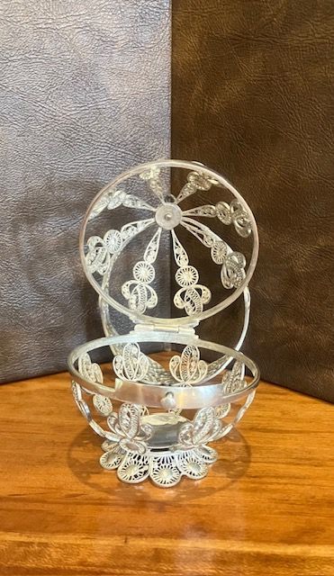 Clear glass decorative bowl with a circular, lace-like lid on a wooden table against a gray-brown background