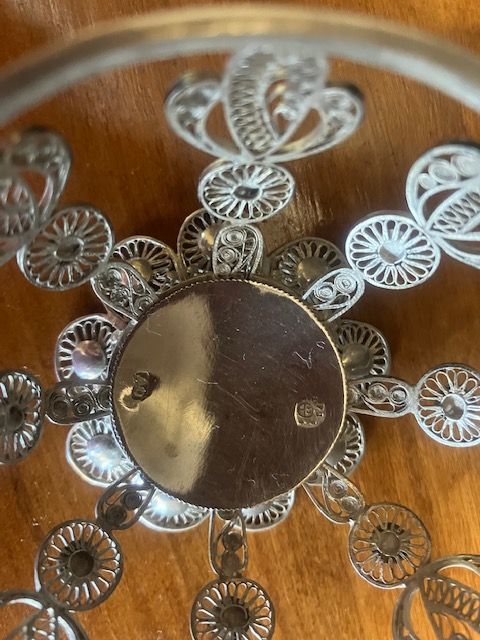Silver floral filigree ornament with a round dark center on a warm wooden background
