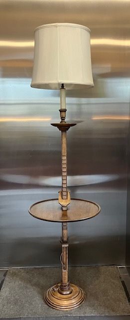 Tall brass floor lamp with cream shade and round glass side table, shown against a metallic background