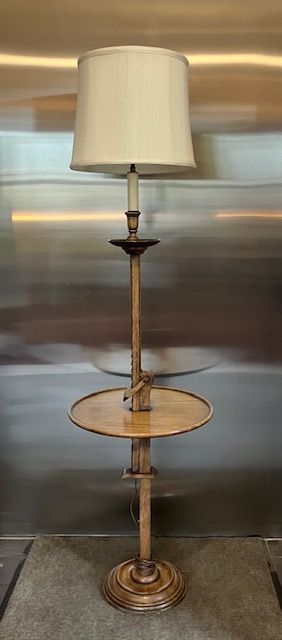 Tall brass floor lamp with a cream shade and round glass side table shelf on a metallic backdrop