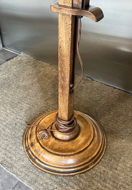 Wooden pedestal floor lamp base with cord, on a carpeted floor against a wall