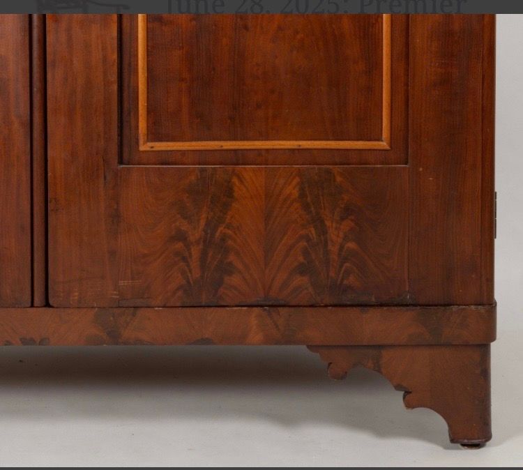 Close-up of a polished wooden cabinet with a decorative lower edge and foot on a light background