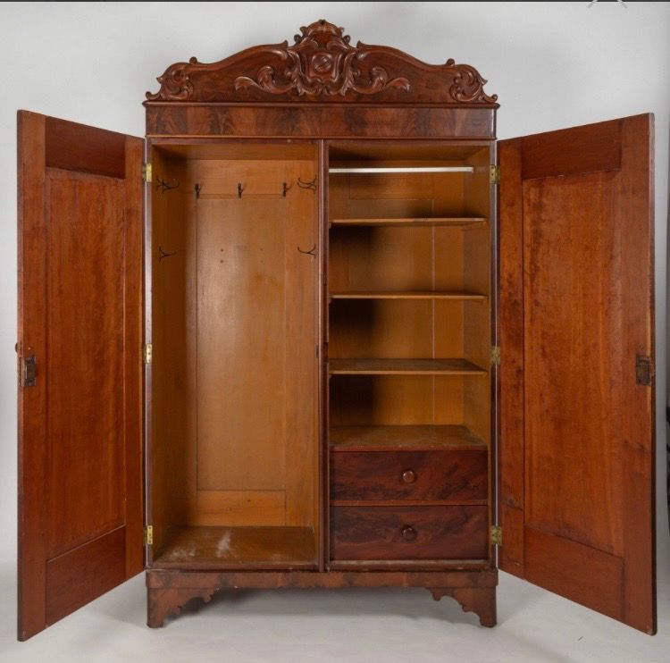 Open antique wooden wardrobe with carved top, shelves, drawers, and hanging space.