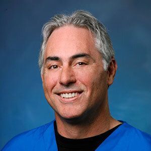 A man in a blue scrub is smiling for the camera.