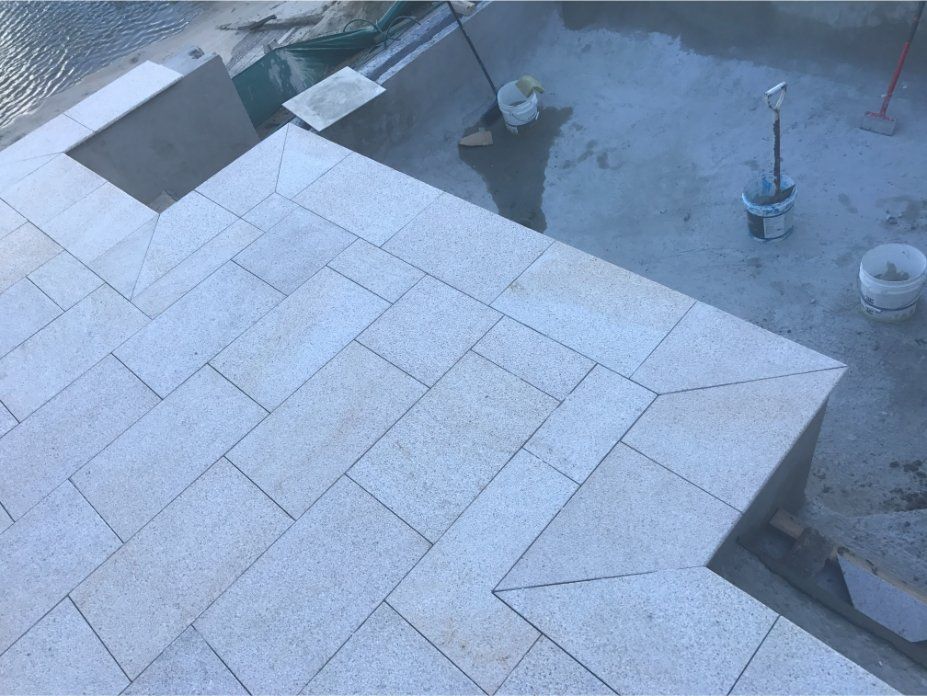 Stone tiling on a patio with steps, buckets and tools, viewed from above, in an outdoor setting.