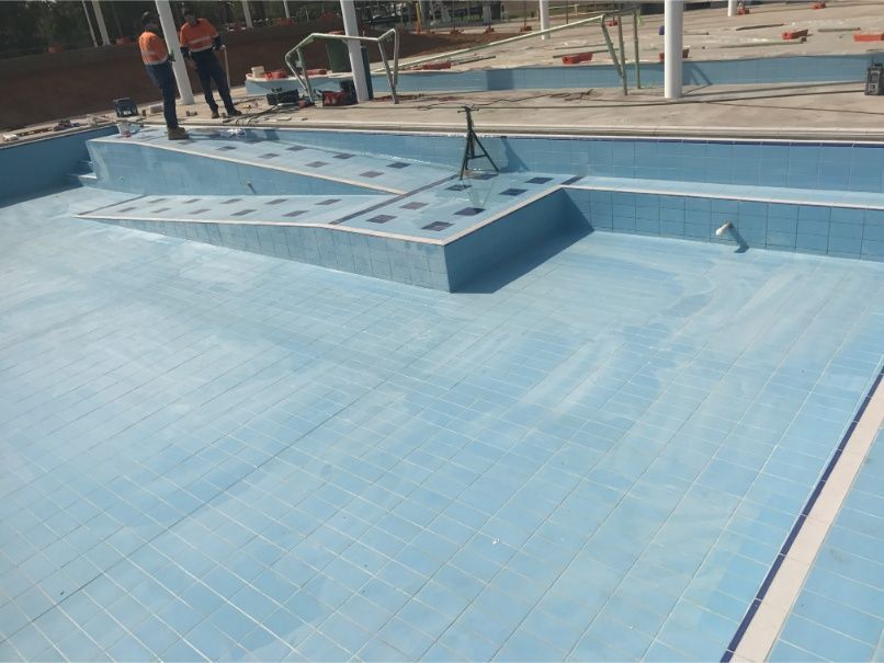 A partially tiled swimming pool under construction. Two workers stand nearby. Blue tile. — Worrall Tiling in South Kempsey, NSW
