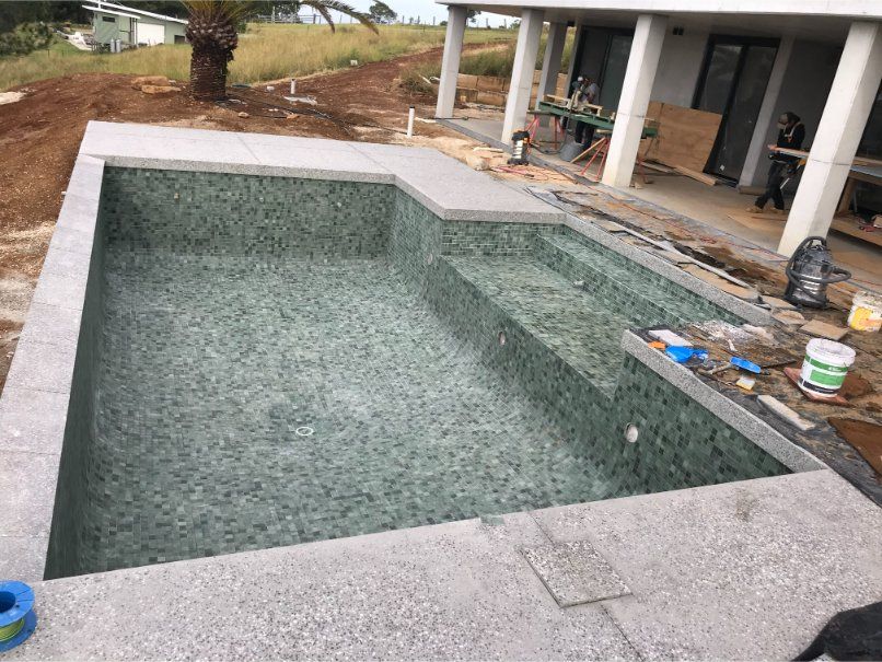 A pool under construction with green tile interior, gray concrete borders, and a house in the background. — Worrall Tiling in South Kempsey, NSW