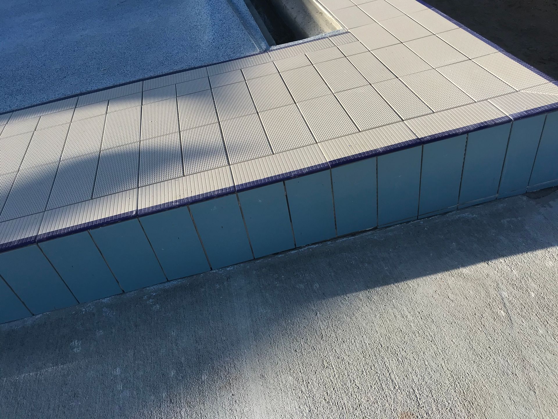 A pool deck made of light gray tiles, with a blue pool and wall. — Worrall Tiling in South Kempsey, NSW