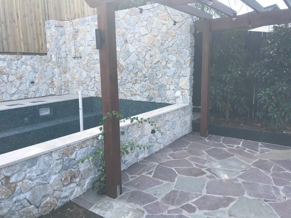Stone-walled pool with wood pergola and flagstone patio; lush greenery. — Worrall Tiling in South Kempsey, NSW