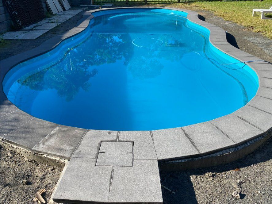Swimming Pool Filled With Blue Water, Surrounded by Gray Stone — Worrall Tiling in South Kempsey, NSW