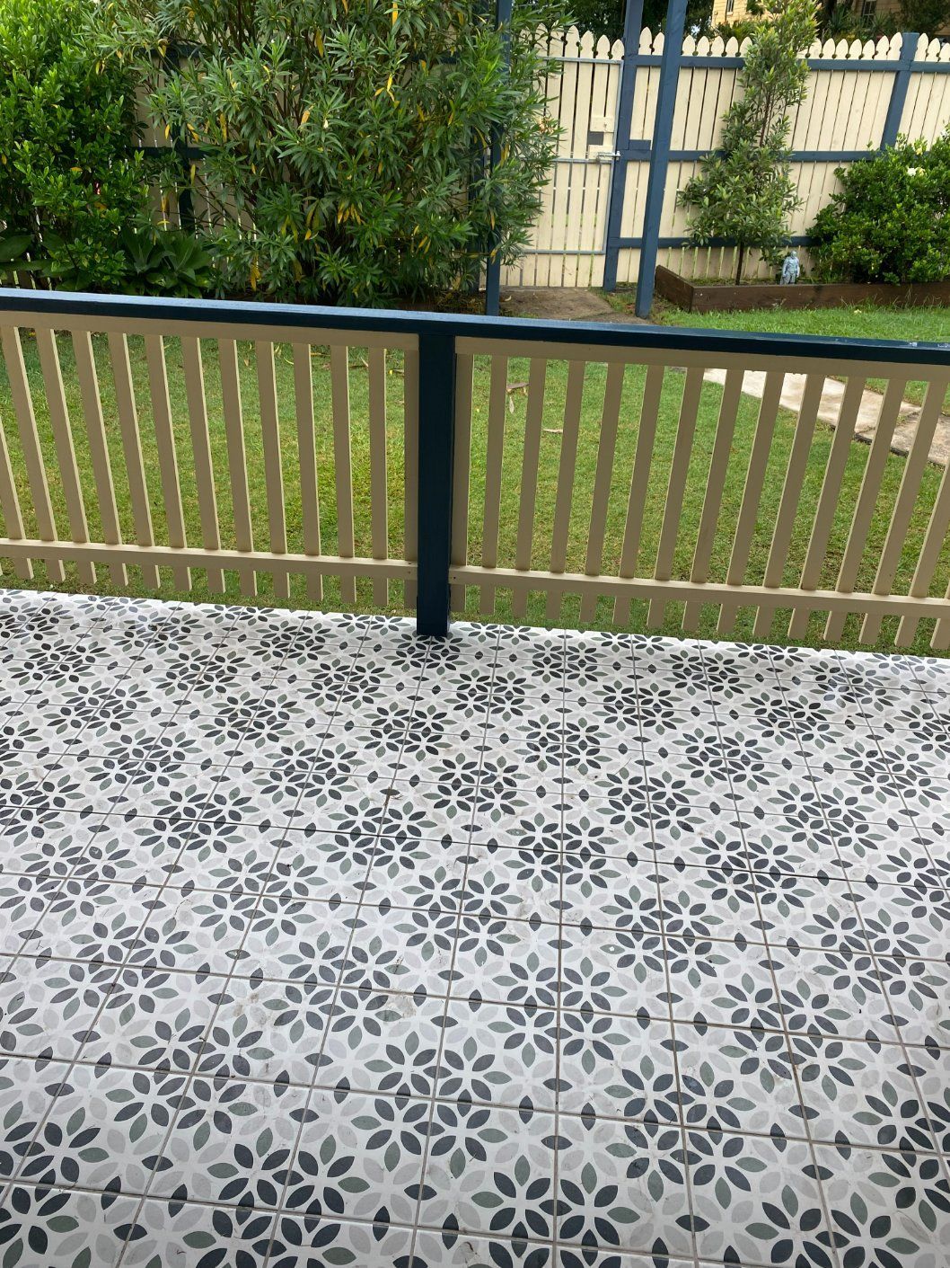 Patterned floor on a veranda with light green railing, overlooking a backyard with a fence. — Worrall Tiling in South Kempsey, NSW