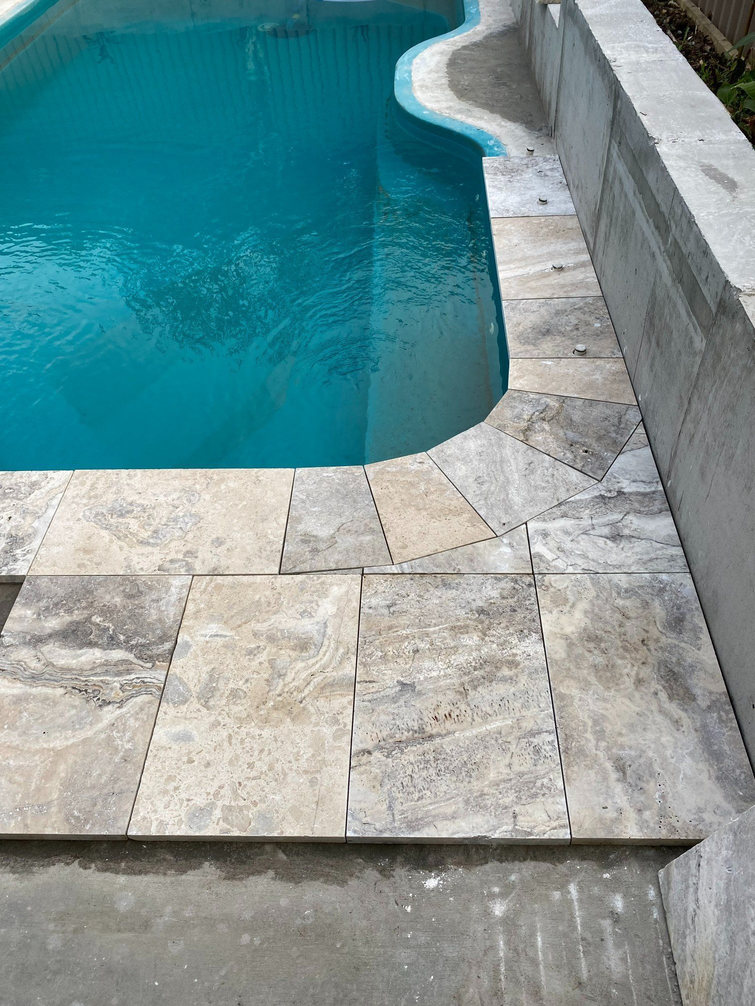 Swimming pool edge with stone tiles, blue water, and concrete wall. — Worrall Tiling in South Kempsey, NSW