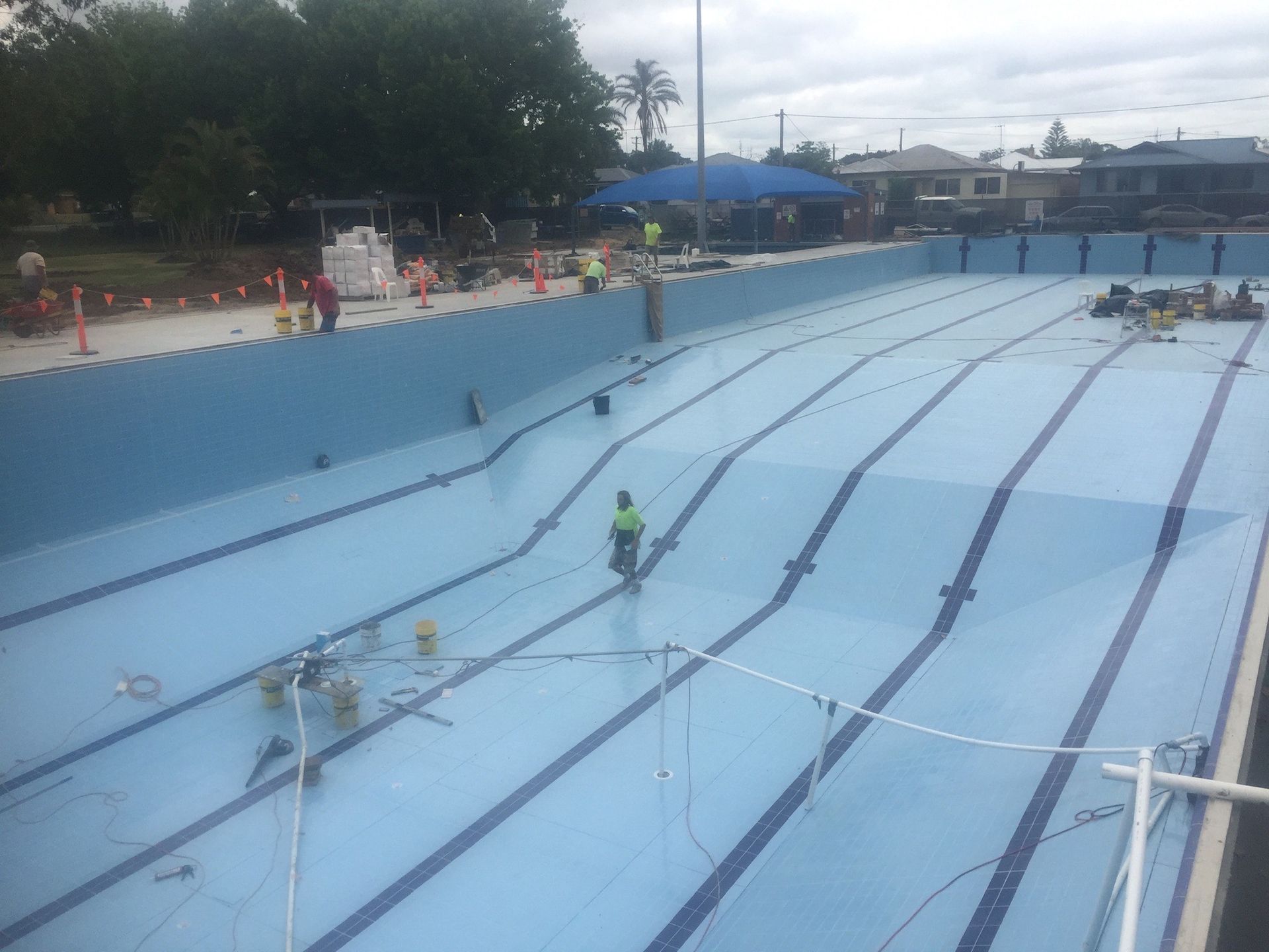 Empty, blue swimming pool undergoing renovations. Workers are present. — Worrall Tiling in South Kempsey, NSW