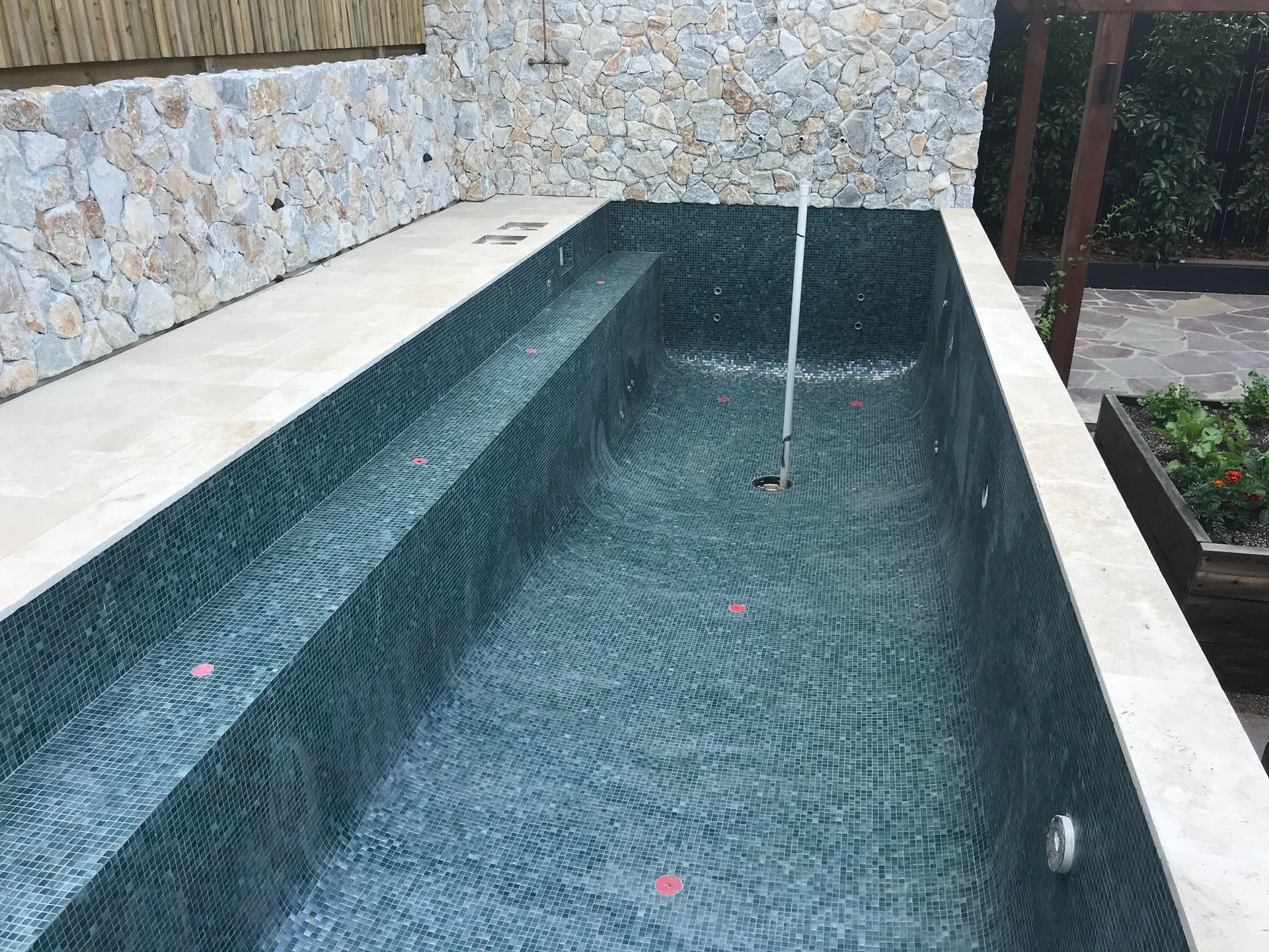 Rectangular dark tiled pool, partially filled with water, next to a stone wall and tan deck. — Worrall Tiling in South Kempsey, NSW