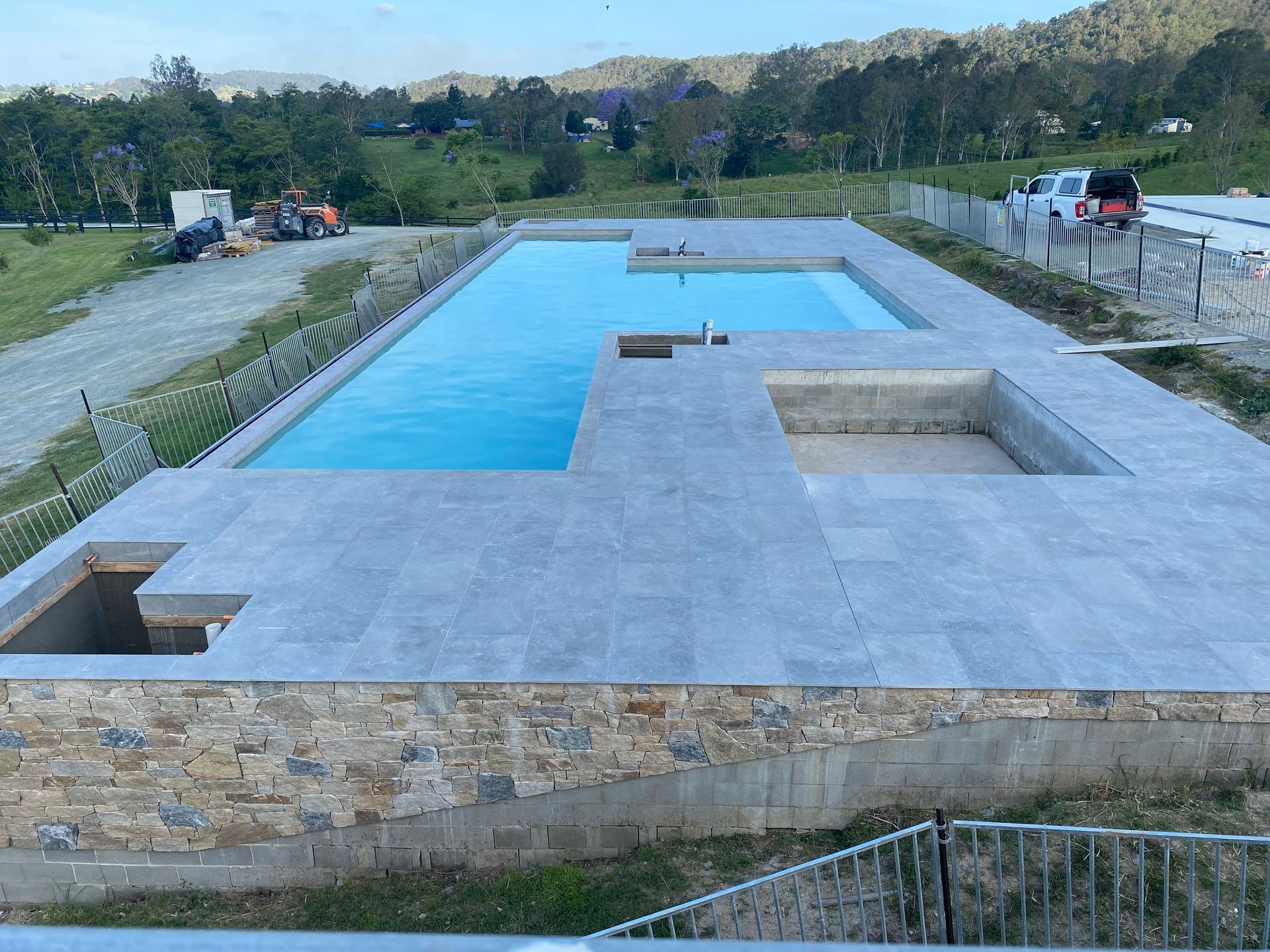 A partially completed rectangular pool with light blue water and stone patio, set against a rural landscape. — Worrall Tiling in South Kempsey, NSW