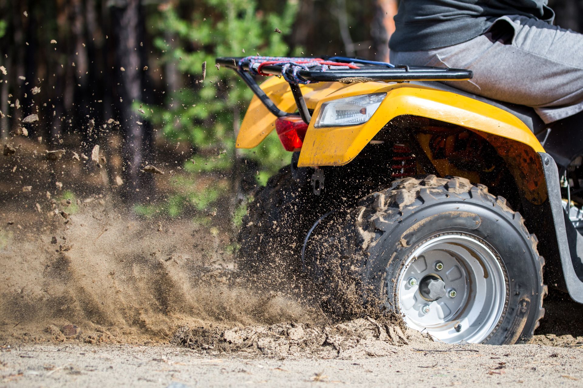 Yellow ATV splashing mud on a dirt trail, with a rider partially visible.