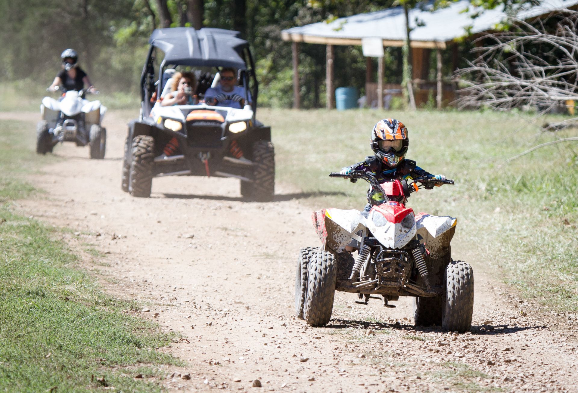 Yellow ATV splashing mud on a dirt trail, with a rider partially visible.