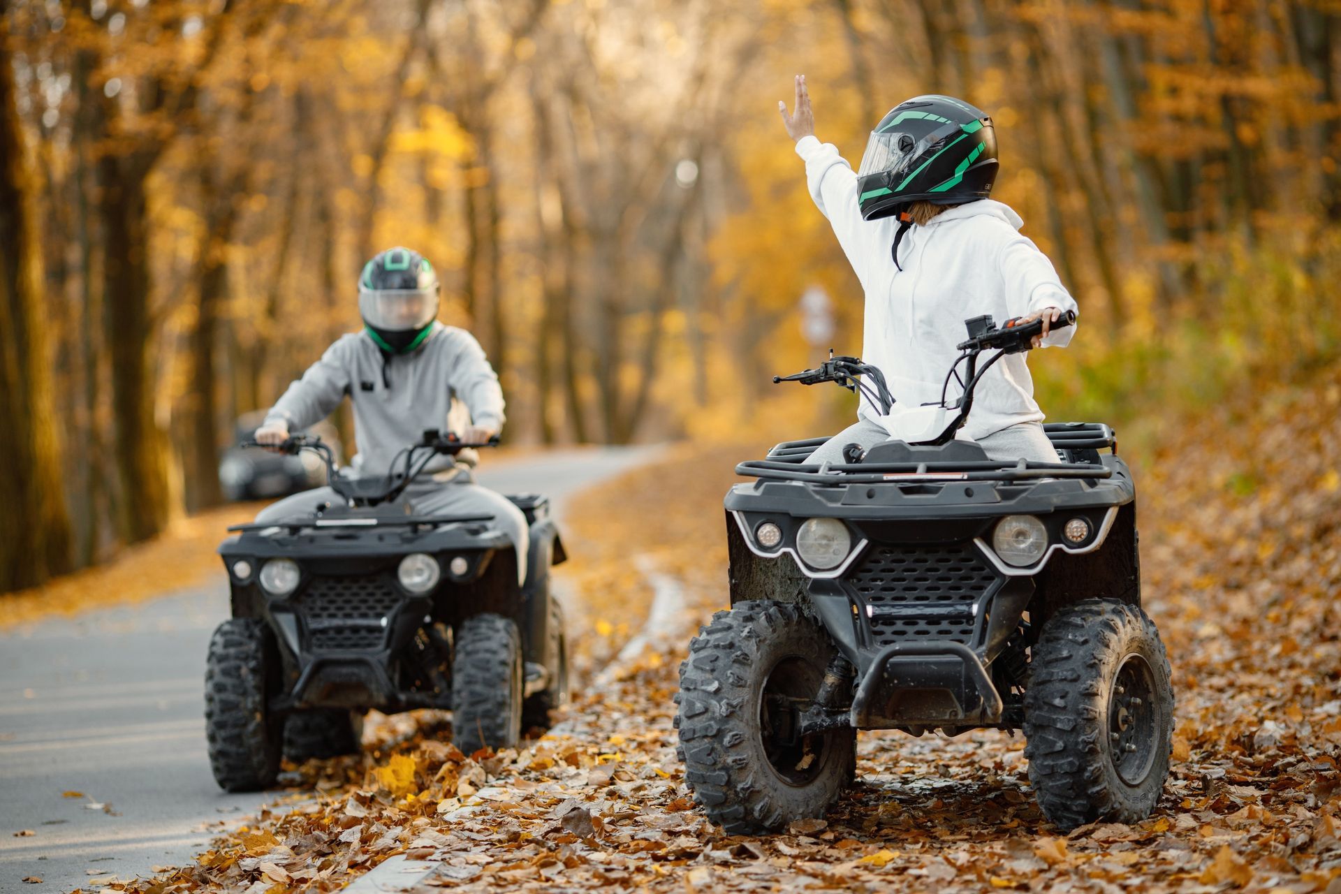 Two ATV riders on a leaf-covered forest trail in autumn