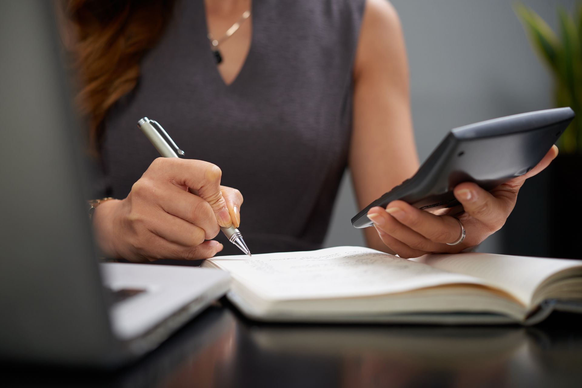 Woman in gray dress using a calculator and writing in a notebook.