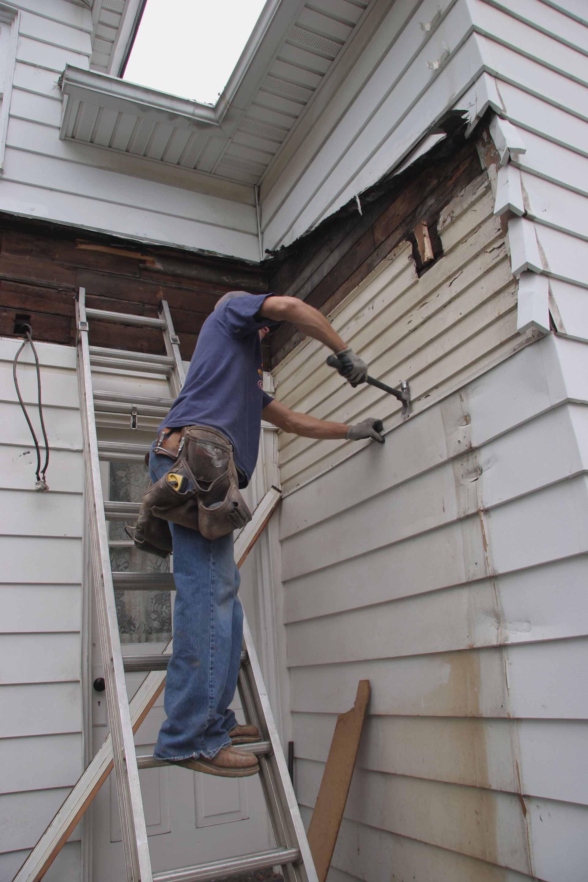 A man is standing on a ladder working on the side of a house.