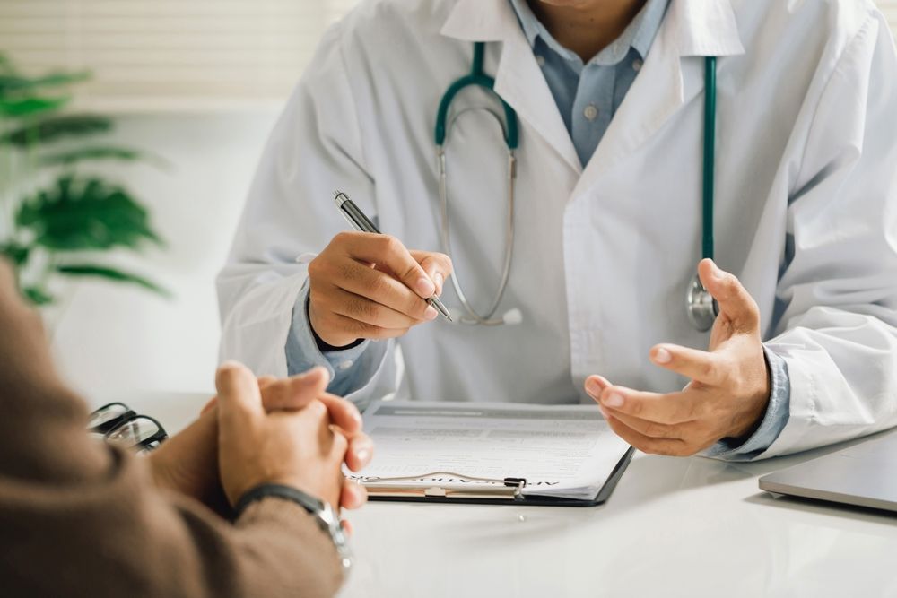 Doctor in white coat with stethoscope consulting a patient at a desk.