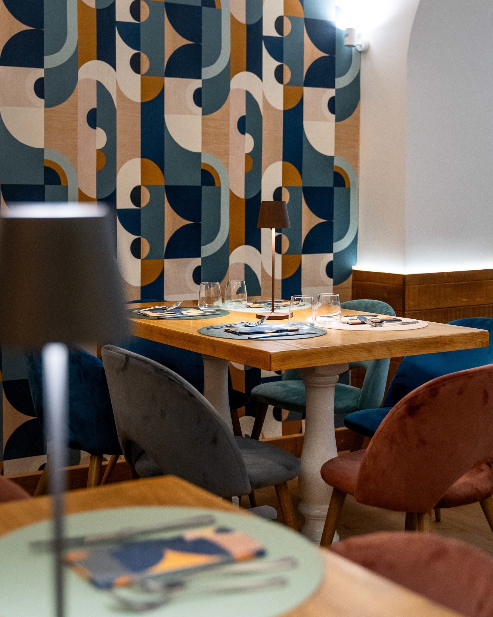 Accogliente angolo caffè con tavolini decorati alle pareti, tavolo in legno e sedie imbottite colorate.