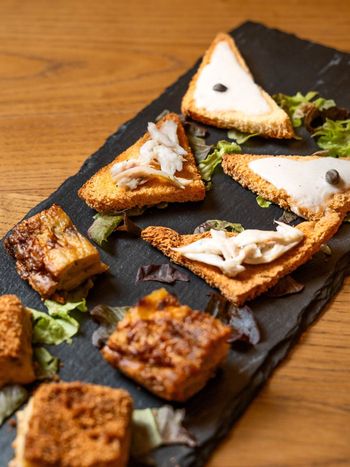 Antipasti di pane tostato su un piatto di ardesia con verdure e salsa a filo.