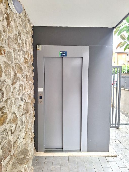 Ascensore chiuso in una nicchia d'ingresso di un edificio in pietra e grigio