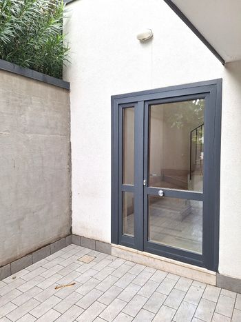 Piccolo patio pavimentato accanto a un muro bianco con porta e finestra laterale in vetro grigio scuro.