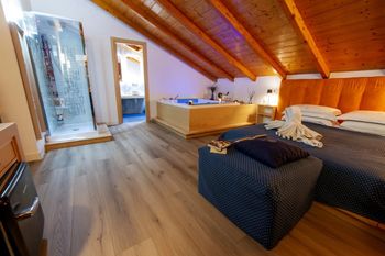 Accogliente camera da letto mansardata con soffitto in legno, letto matrimoniale, pouf decorato e box doccia in vetro.