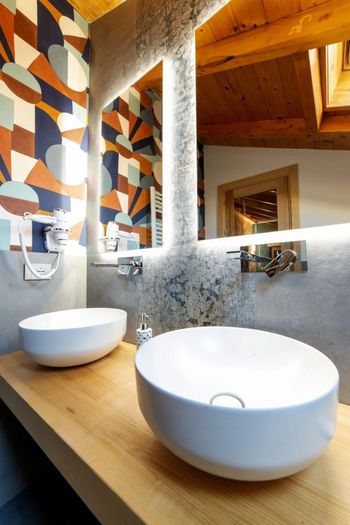 Bagno moderno con due lavabi a ciotola bianchi, piano in legno, piastrelle a parete decorate e soffitto in legno.