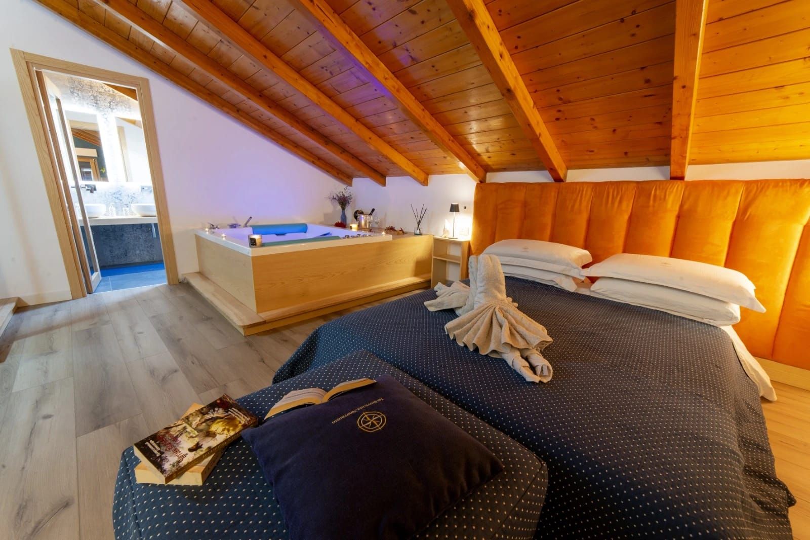Accogliente camera da letto mansardata con soffitto con travi a vista, testiera arancione e due letti vicino a una porta aperta.