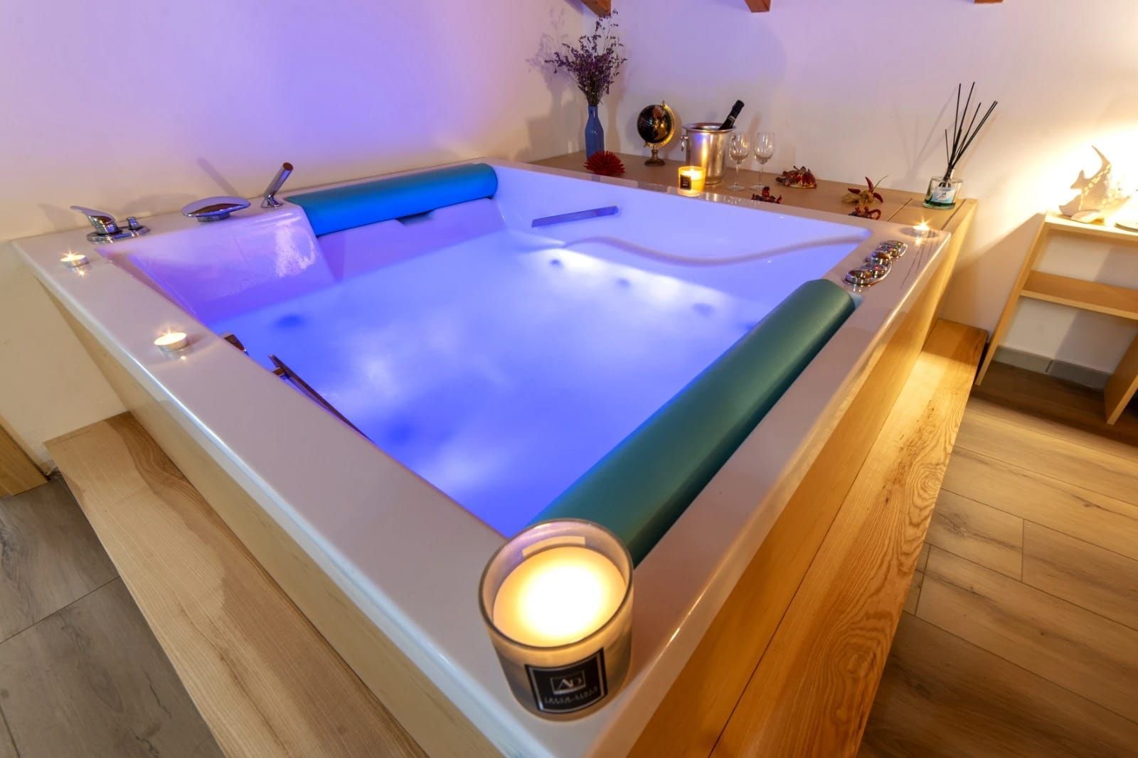 Vasca idromassaggio interna illuminata con acqua blu-violacea e candele in una stanza simile a una spa.