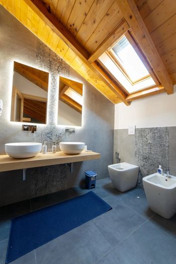Bagno moderno con lucernario, soffitto in legno, doppio lavabo, specchi e WC e bidet separati.