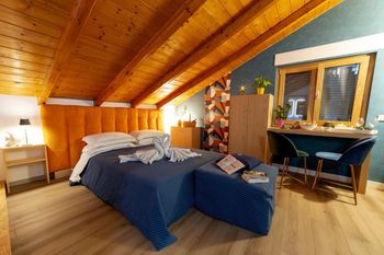 Accogliente camera da letto mansardata con soffitto in legno, copriletto blu e una piccola scrivania vicino alla finestra.