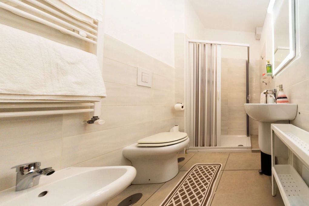 Bagno luminoso con WC, lavabo, bidet, box doccia e piastrelle beige.