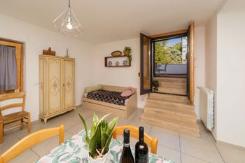 Luminosa camera da letto con letto, armadio, sedia, tavolo e porta finestra che si apre sul balcone con vista sugli alberi.